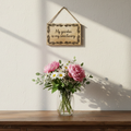 Vase of flowers on a wooden surface with a hanging sign reading 'My garden is my sanctuary' on a light background